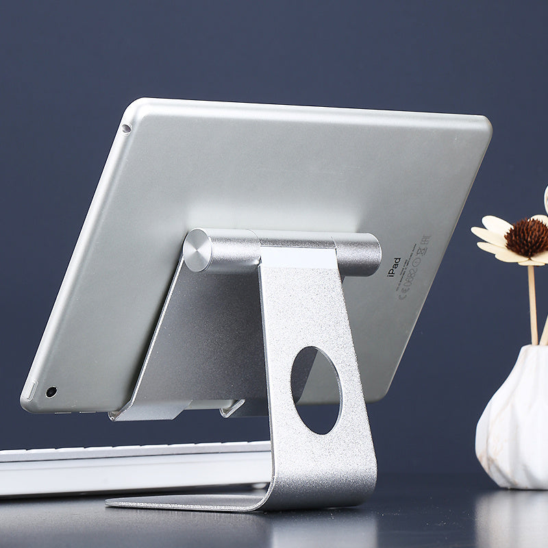 Silver tablet stand holding a tablet on a dark surface with a vase of flowers in the background